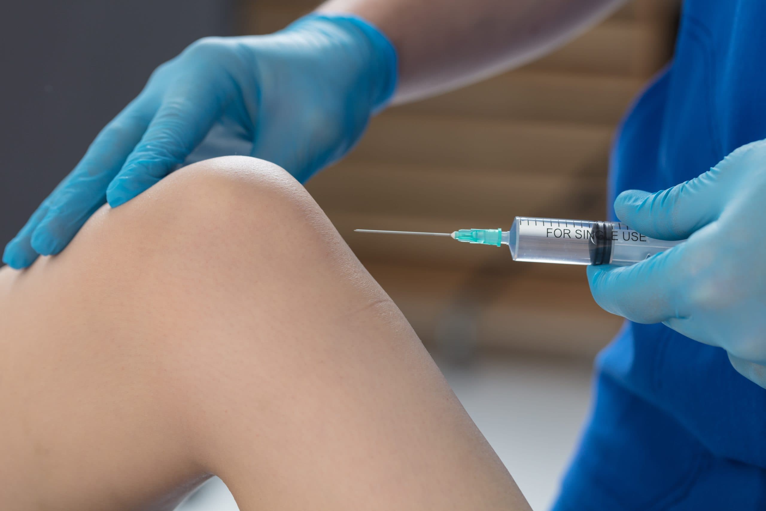 Blue-gloved clinician performing a knee injection procedure